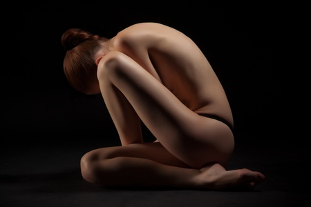 Nude red-haired girl sitting over dark background, studio shotの写真素材