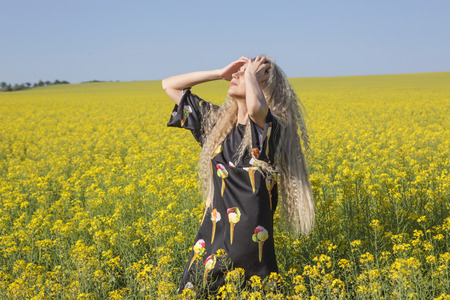 Summer heat. Girl posing in a yellow blooming field. Outdoor shot.