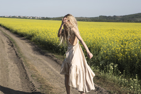 Running away and looking back blonde girl. Country landscape. Yellow blooming fields.の写真素材