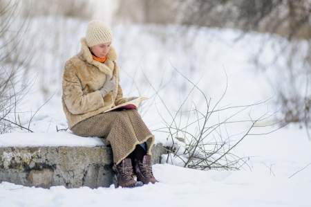Woman sitting on a bench and reading a book in winter  Snow の写真素材