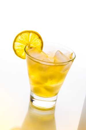 A fresh and tasty cocktail with alcohol and lemon on a glass table with yellow reflectionの写真素材