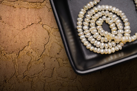 Natural pearls necklace in a little black ceramic cup, on a textured background, with space for copy textの写真素材