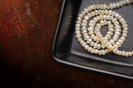 Natural pearls necklace in a little black ceramic cup, on a textured background, with space for copy textの写真素材