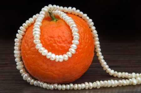 Natural pearls necklace rolled around an orange tangerine, put on a wooden teak tableの写真素材