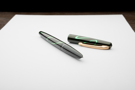 A black and green open fountain pen on a white sheet of paper, on a wooden deskの写真素材