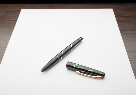 A black and green open fountain pen on a white sheet of paper, on a wooden deskの写真素材