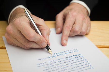 A businessman writing with a fountain pen on a white paper set on a wooded deckの写真素材
