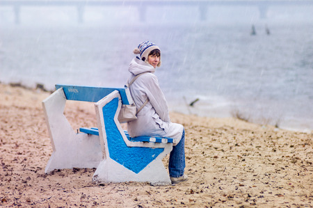 A woman sitting on a bench close to the river, in autumn under the rainの写真素材