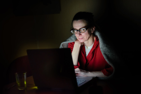 A senior woman using a computer in the dark during a cold winter eveningの写真素材