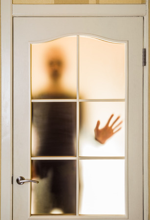 Silhouette of an unknown man in black  seen through a closed glass door, like a ghost or an alienの写真素材