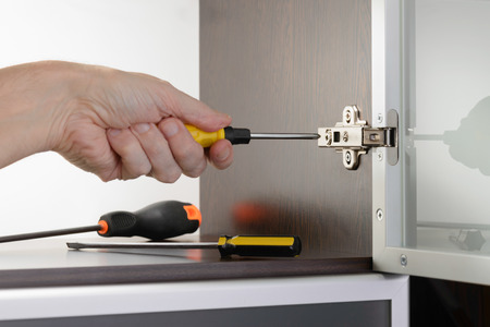 A man uses a screwdriver to adjust a concealed hinge fixed on a modern cabinet with a glass doorの写真素材