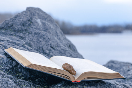 Stone on an open book put on a granite stone under the rain close to the riverの写真素材