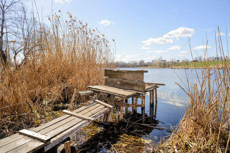 A wooden pontoon close to the lake is waiting for the fisherman under a blue and cloudy skyの写真素材