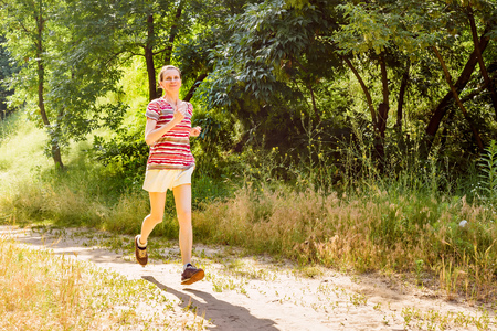 A happy senior woman is running with the sun in backlight, toward the shadow, in the forest during a warm summer dayの写真素材