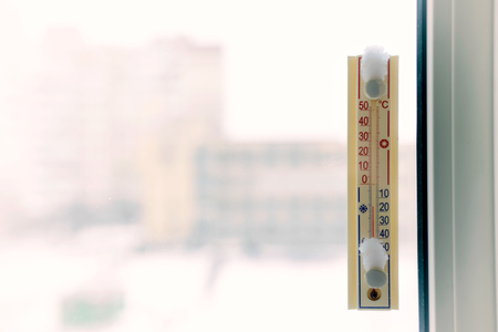 A thermometer, fixed out of the window, shows that it is minus seventeen degree celsius outdoor, while it is warm inside the roomの写真素材