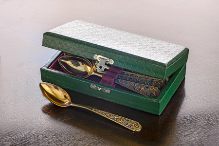 An antique golden spoons case on a wooden table.の写真素材