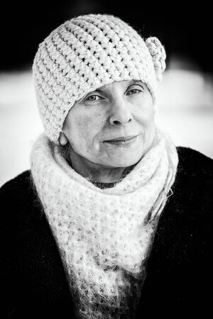 A winter portrait of a senior adult woman wearing a wool cap and a scarf, with a snow backgroundの写真素材