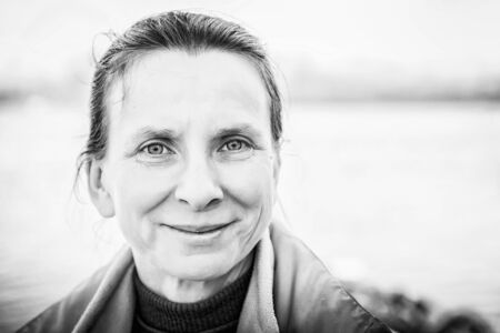 A warm black and white portrait of a nice senior woman close to the riverの写真素材
