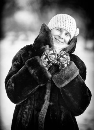 A winter portrait of a smiling senior adult woman wearing a wool cap, a scarf and colored gloves, with a snow backgroundの写真素材