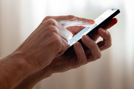 Man typing with the finger on the touch screen of a black smartphone close to the window with closed...