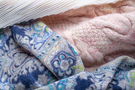Soft folds of a warm pink knitted woolen pullover and a blue decorated scarf with a white pleated...