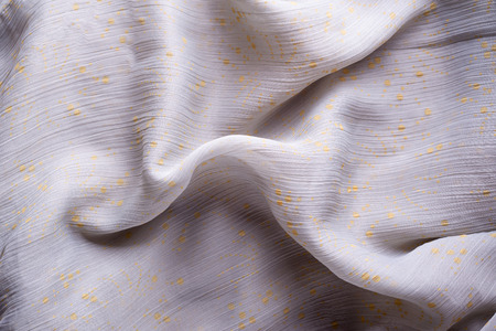 Soft folds of a light pink synthetic fabric texture with yellow gold ornaments to be used as backgroundの写真素材