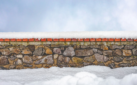 Stone wall covered by fresh snow in winter. A clear sky with soft white clouds appears in the backgroundの写真素材