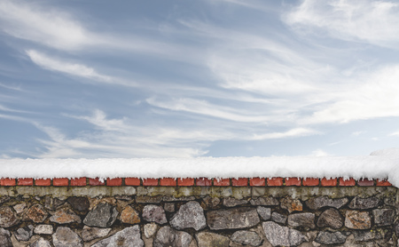Stone wall covered by fresh snow in winter. A clear sky with soft white clouds appears in the backgroundの写真素材