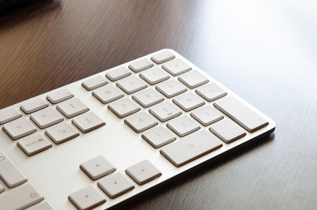 A light gray numeric keyboard on a dark wooden desk tableの写真素材