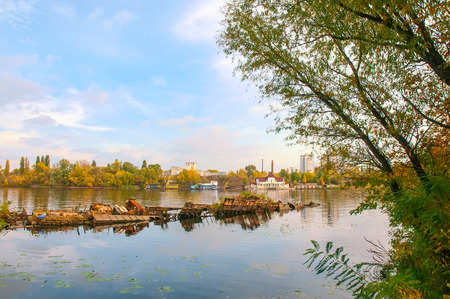 Wrecked boat on the Dnieper river in Kiev, Ukraine, in autumn. In the background, ypou can see an uninhabited floating house. Light clouds float in a pale blue skyの写真素材