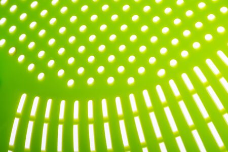 Macro of a green plastic colander, a kitchen utensil to drain pasta, on a white background, creating an abstract texture. Selective focusの写真素材