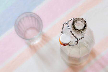 Top view of a glass bottle with a  wire bail clasp ceramic stopper, and a drink glass, on a blue, pink and orange stripped tableclothの写真素材