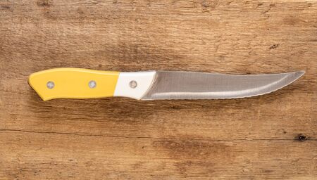 Kitchen knife, with yellow and white handle and steel sawtooth blade on a natural wood background.の写真素材