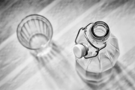 Top view of a glass bottle with a  wire bail clasp ceramic stopper, and a drink glass, on a blue, pink and orange stripped tableclothの写真素材