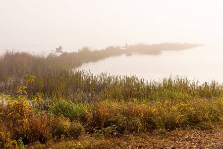 Autumn mist on the Dnieper river, in the morning, in Kiev, Ukraine. Fishermen emerging from the fog are fishing in middle of the reeds.の写真素材