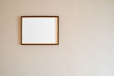 A true antique wooden photo frame with gold ornaments and blank copy space, for insertion of any image, on a wall covered by beige painted wallpaper.の写真素材