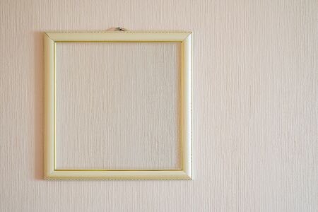 A true modern photo frame with gold ornaments and blank copy space, for the insertion of any image, on a wall covered with beige painted wallpaper.の写真素材