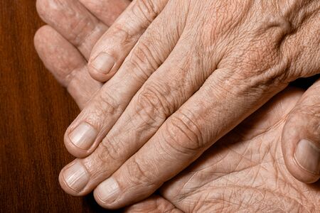 Color photo of senior man crossed hands detail on a dark wooden background