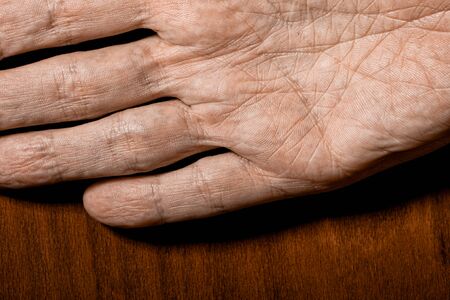 Picture of elderly male hands on a wooden background. Detail of the palm of the hand.の写真素材