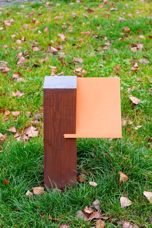 Blank orange wooden board for information and indications in the park, with a background of green grass covered by autumn leavesの写真素材