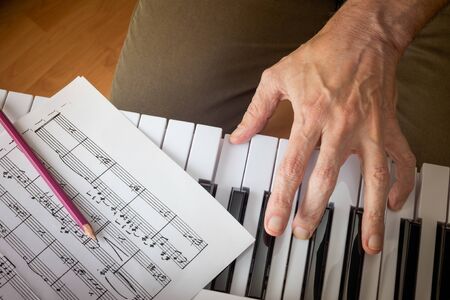 PUBLIC DOMAIN MUSIC SCORE. Close up detail on the hand of a musician composer playing the black and white keys of an electronic  music keyboard and writing notes on the musical stave.の写真素材