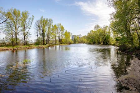 Nice and quiet spring day close to the Dnieper river. Young green leaves are growing on the trees under a tepid sun. Blue water and soft clouds in the sky.の写真素材