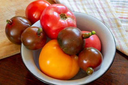 Various kind of tomatoes, yellow, red and black, in an enamel bowl, on a cutting boardの写真素材
