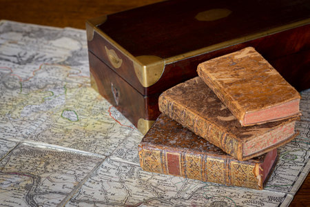 Pile of antique books with a leather cover and golden ornaments, close to a wooden box on an ancient topographic mapの写真素材