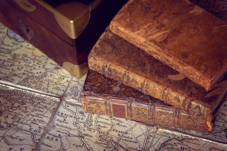 Pile of antique books with a leather cover and golden ornaments, close to a wooden box on an ancient topographic mapの写真素材