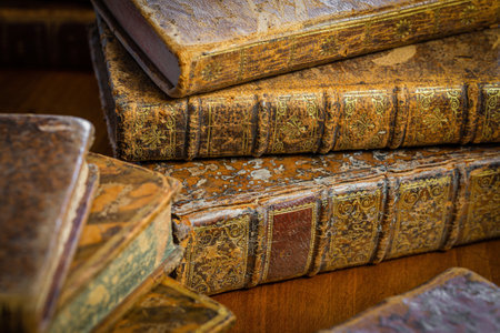 Pile of antique books with a leather cover and golden ornaments on a wooden tableの写真素材