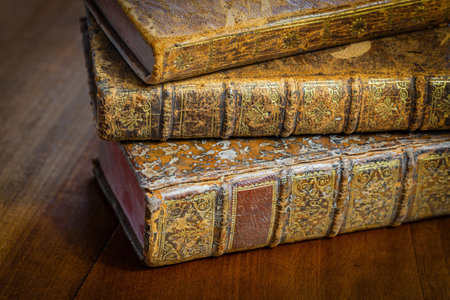 Pile of antique books with a leather cover and golden ornaments on a wooden tableの写真素材