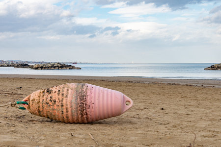 An orange buoy on the Cattolica beach, in Emilia Romagna a regione of Italy, in winter under a cloudy sky. Riccione and Rimini appear in the backgroundの写真素材
