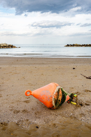 An orange buoy on the Cattolica beach, in Emilia Romagna a regione of Italy, in winter under a cloudy sky.の写真素材