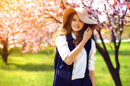 Outdoor portrait of young beautiful fashionable lady posing near flowering tree.の写真素材